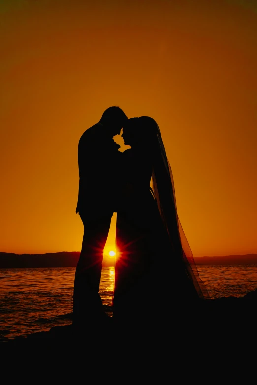 the silhouette of a bride and groom on a beach during sunset