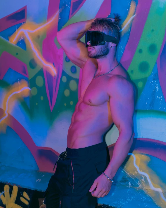 the shirtless man stands in front of a colorful background wearing 3d glasses