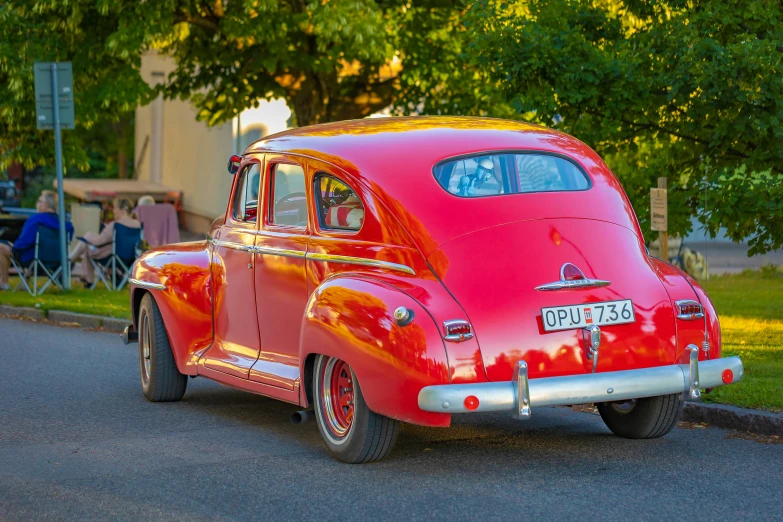 an old red classic car is driving down a country road