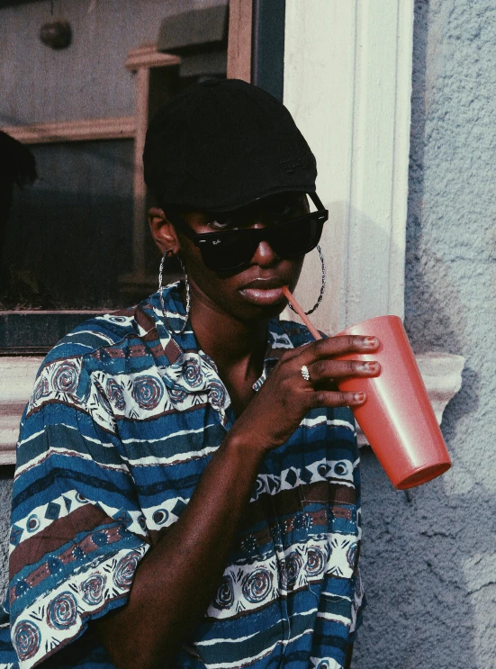 a person in sunglasses and a shirt holds an orange cup