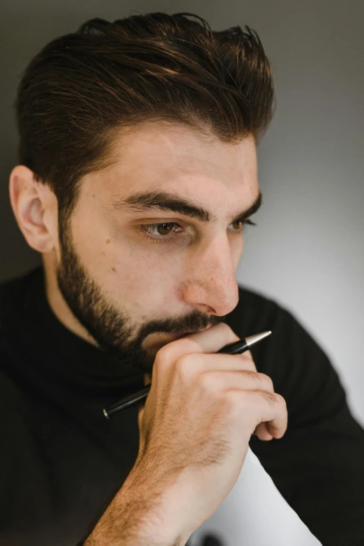 a bearded man in a black shirt holding a pen to his face