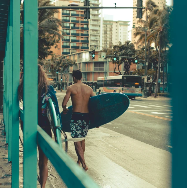 two people carrying surfboards and walking on the sidewalk