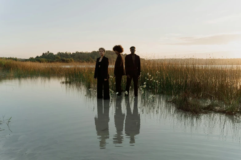 three people standing in front of water with tall grass