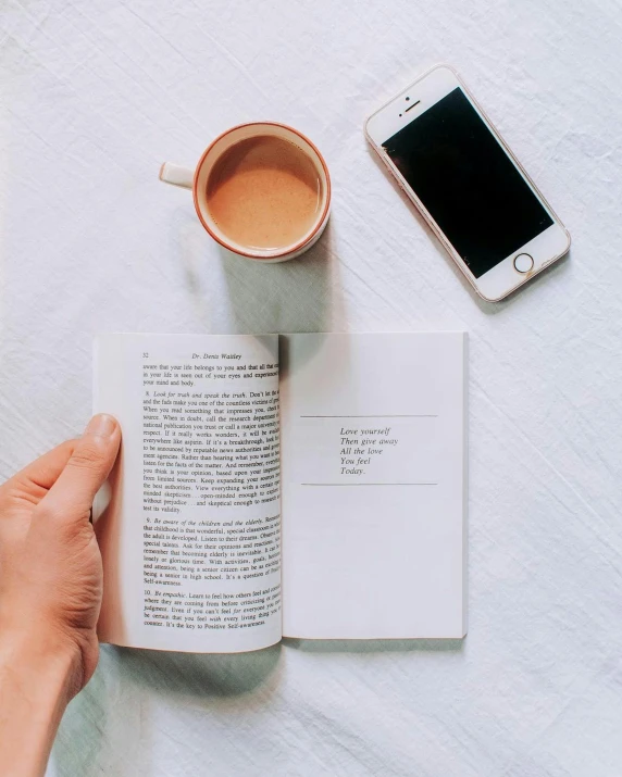 a person's hand holding a book while reading a novel