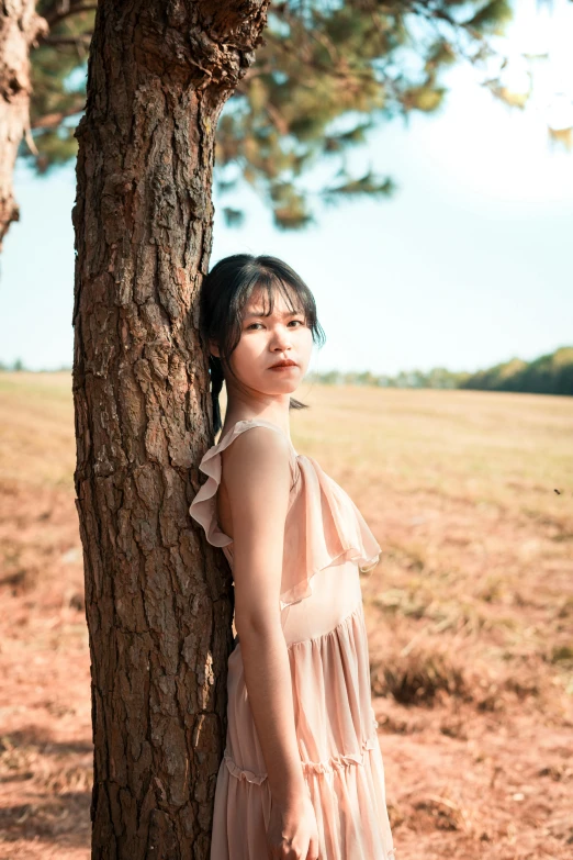 the young woman is posing near a tree