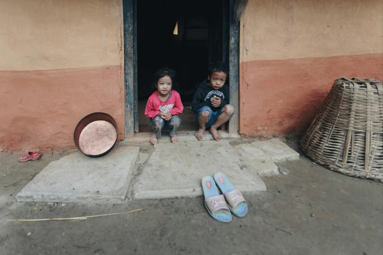 two children sit in the open doorway to a house