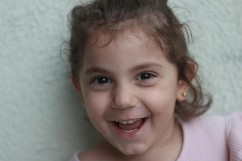 small child smiles in front of a white wall