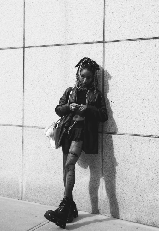 a woman is leaning up against a wall while looking at her cell phone