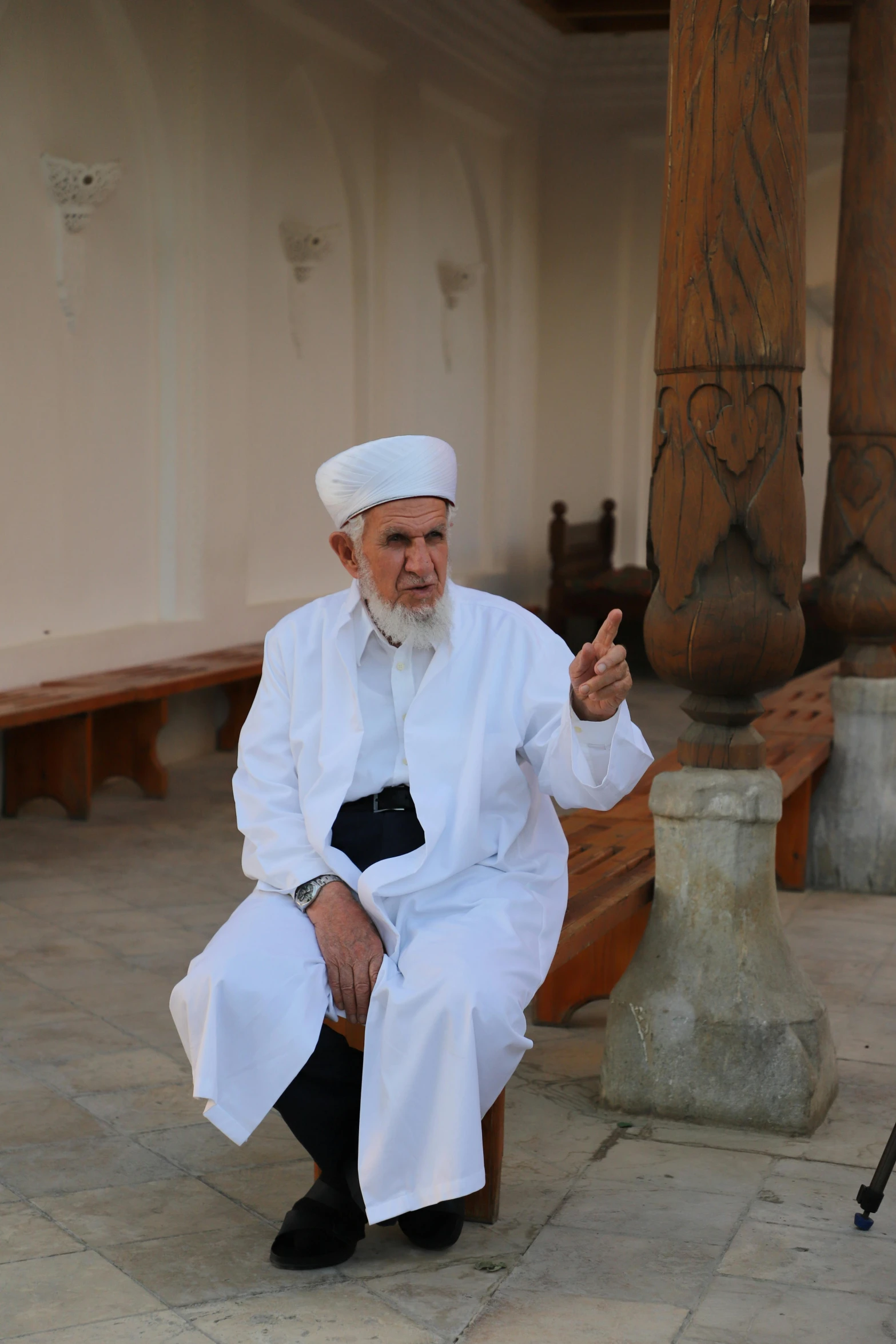 an old man in white robe sitting next to a wooden post