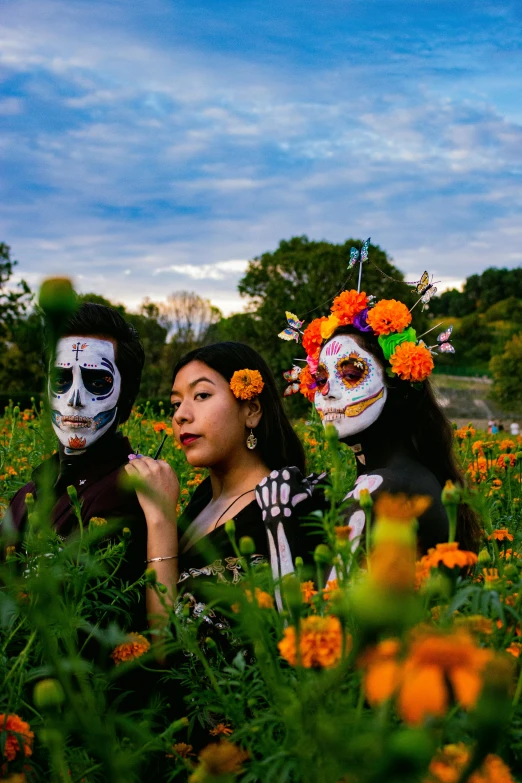 three people with painted faces pose in a flowery field