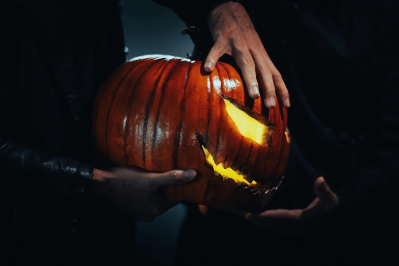 two hands holding a carved pumpkin with both of their hands