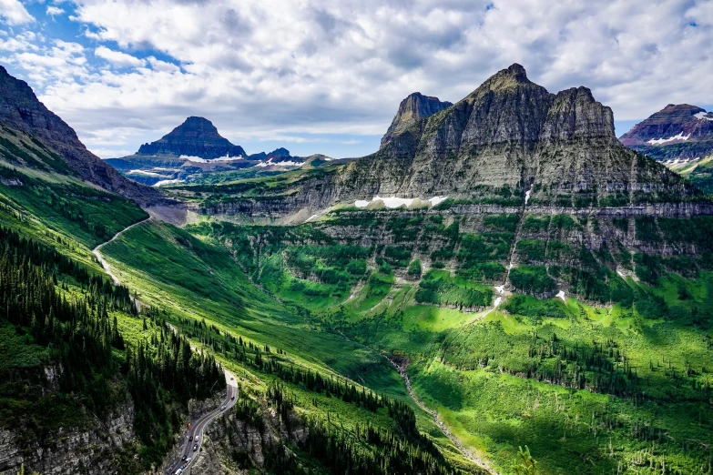 a mountain scene with green vegetation and a road leading to some peaks