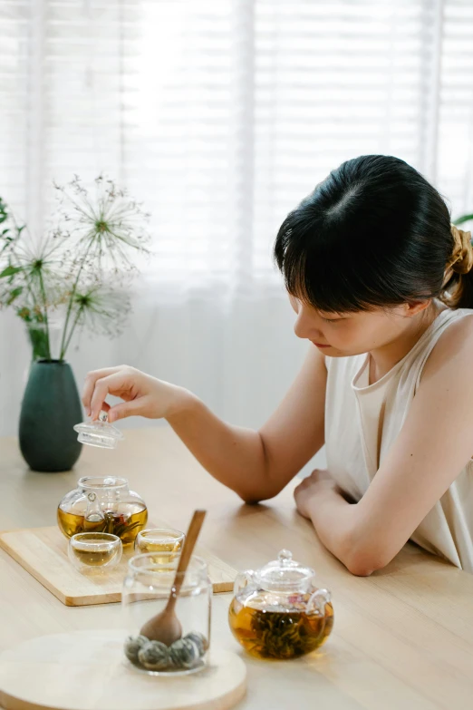 a young woman sitting at a wooden table full of tea