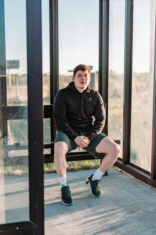 a man sitting on a wooden bench next to tall windows