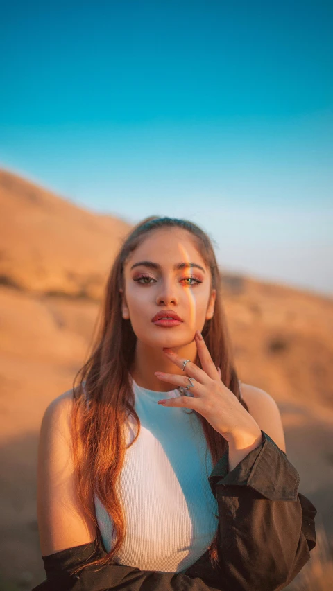 a woman poses with her hand on her face in a desert area