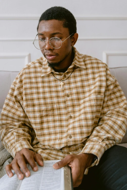 a man sitting on a couch with his head turned towards the camera and reading a book