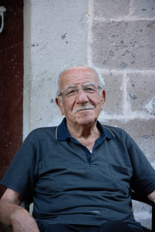 an old man sits in a chair in front of a brick wall