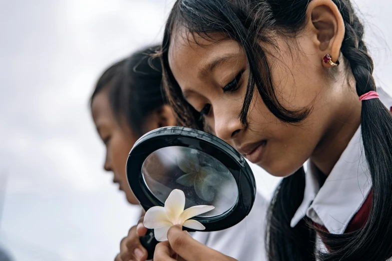 an indian girl looking through a magnifying glass with a flower in front of her