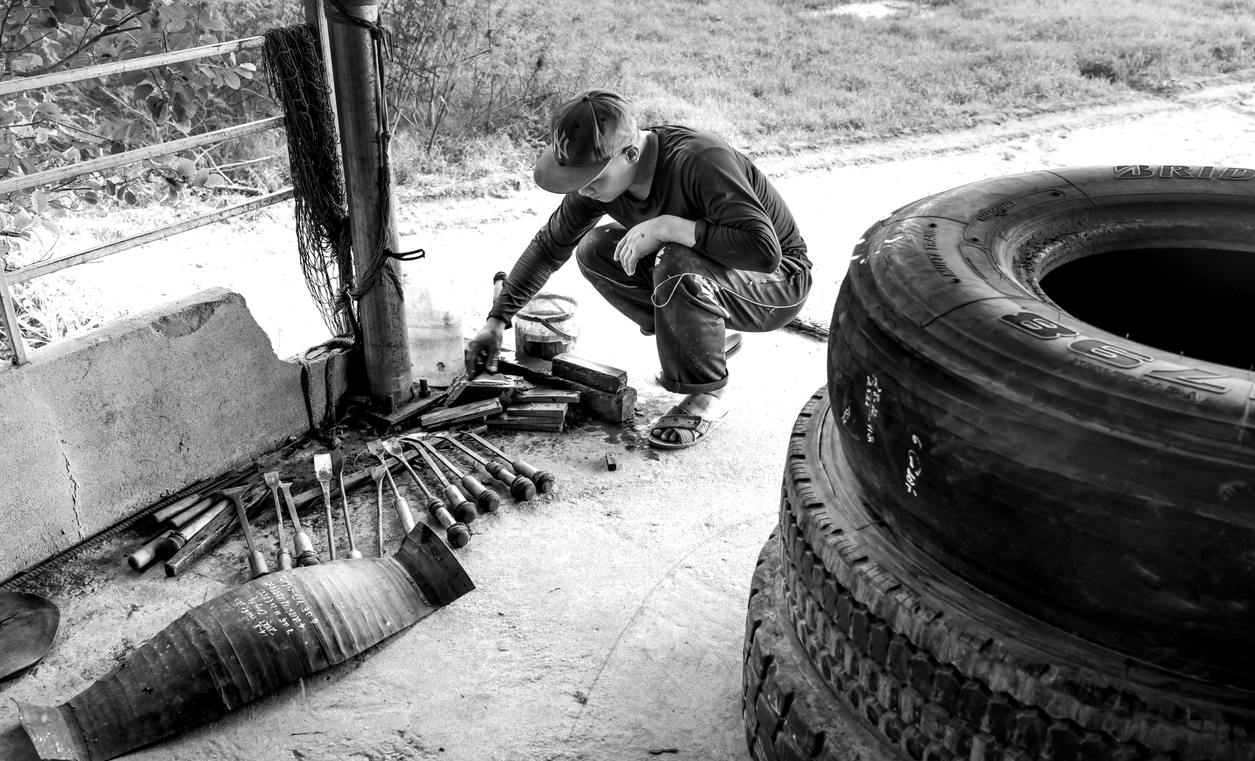 a man in grey jacket kneeling on ground next to tire and other tires