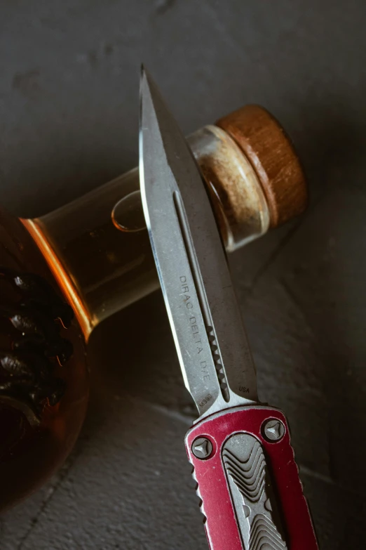 a red and black handled knife next to a bottle