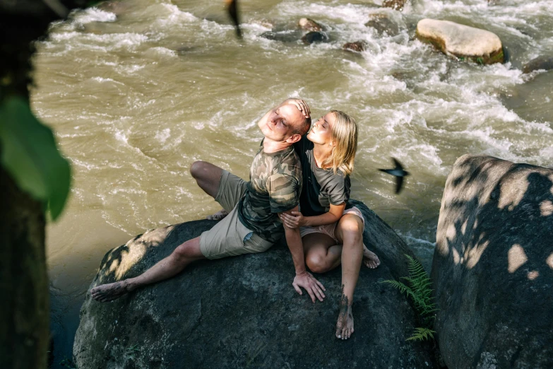 the couple is sitting on a rock near the water