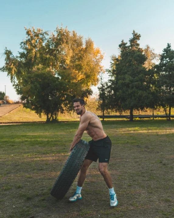 a man in black trunks and blue sneakers holds a skateboard