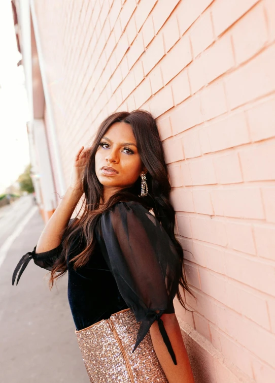 a woman leaning against a brick wall and posing for the camera