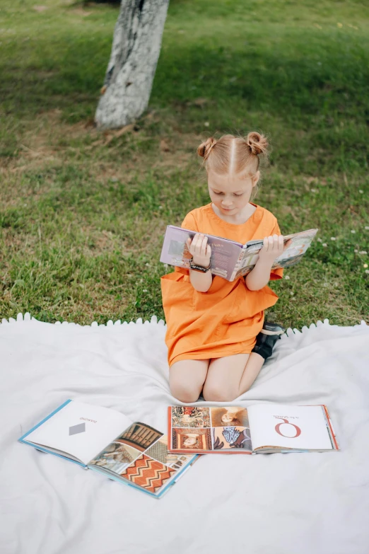 a little girl sitting on a blanket looking at books