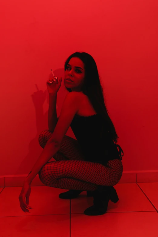 a beautiful young woman kneeling down next to a red wall