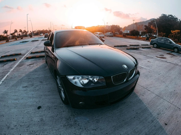 a black bmw parked in a parking lot with the sun setting behind it