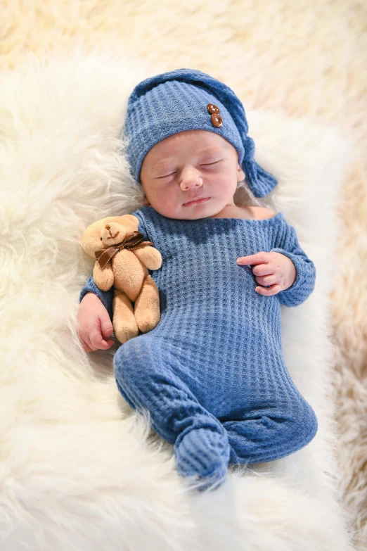 a small baby sleeping on a white blanket with a teddy bear