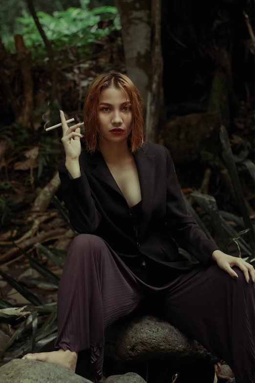 woman smoking cigarette sitting in a forest with a cross on her finger