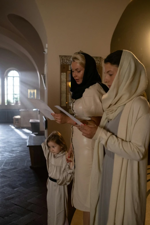 three women wearing robes are standing around with paper