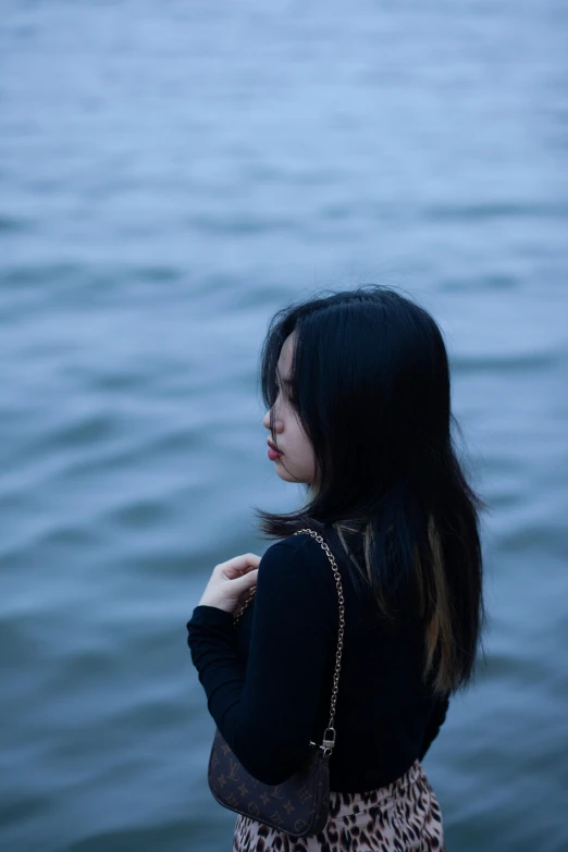 a woman stands next to the ocean with her hands folded