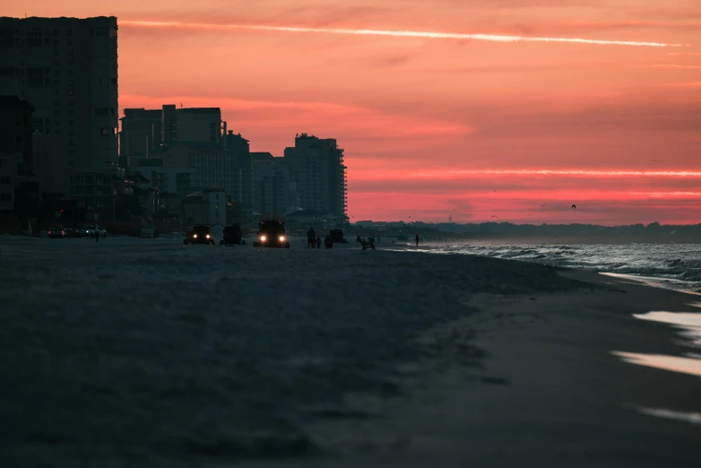 people are walking on the beach next to buildings at dusk