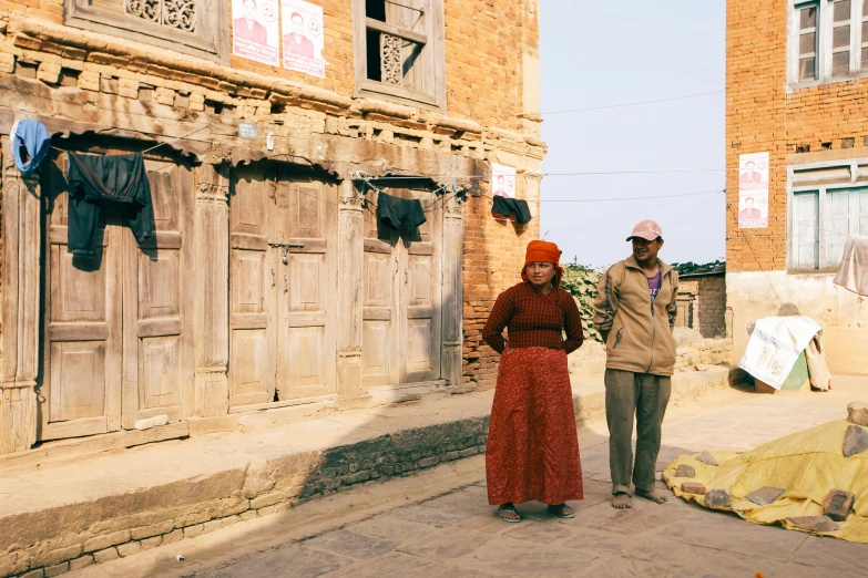 two people are standing near old buildings with clothing drying on a line