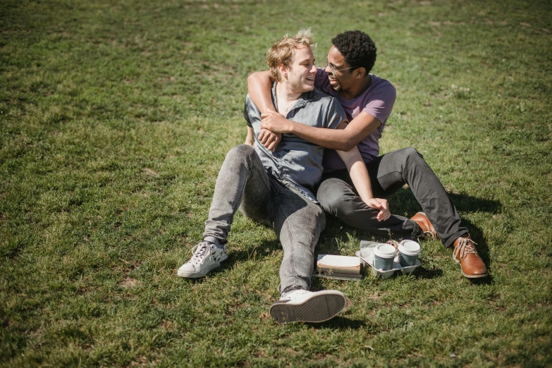 two people sitting on the grass with their arms around each other