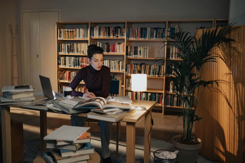 man reading a book while sitting in front of an open laptop computer