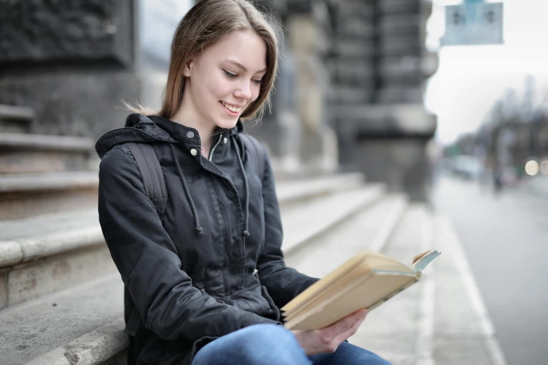 a woman sitting on the side of a road reading a book