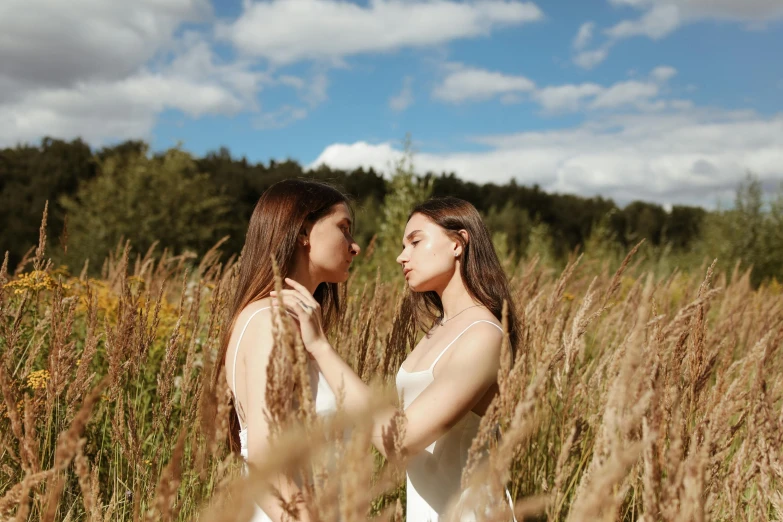 two young women standing next to each other in a field of tall grass