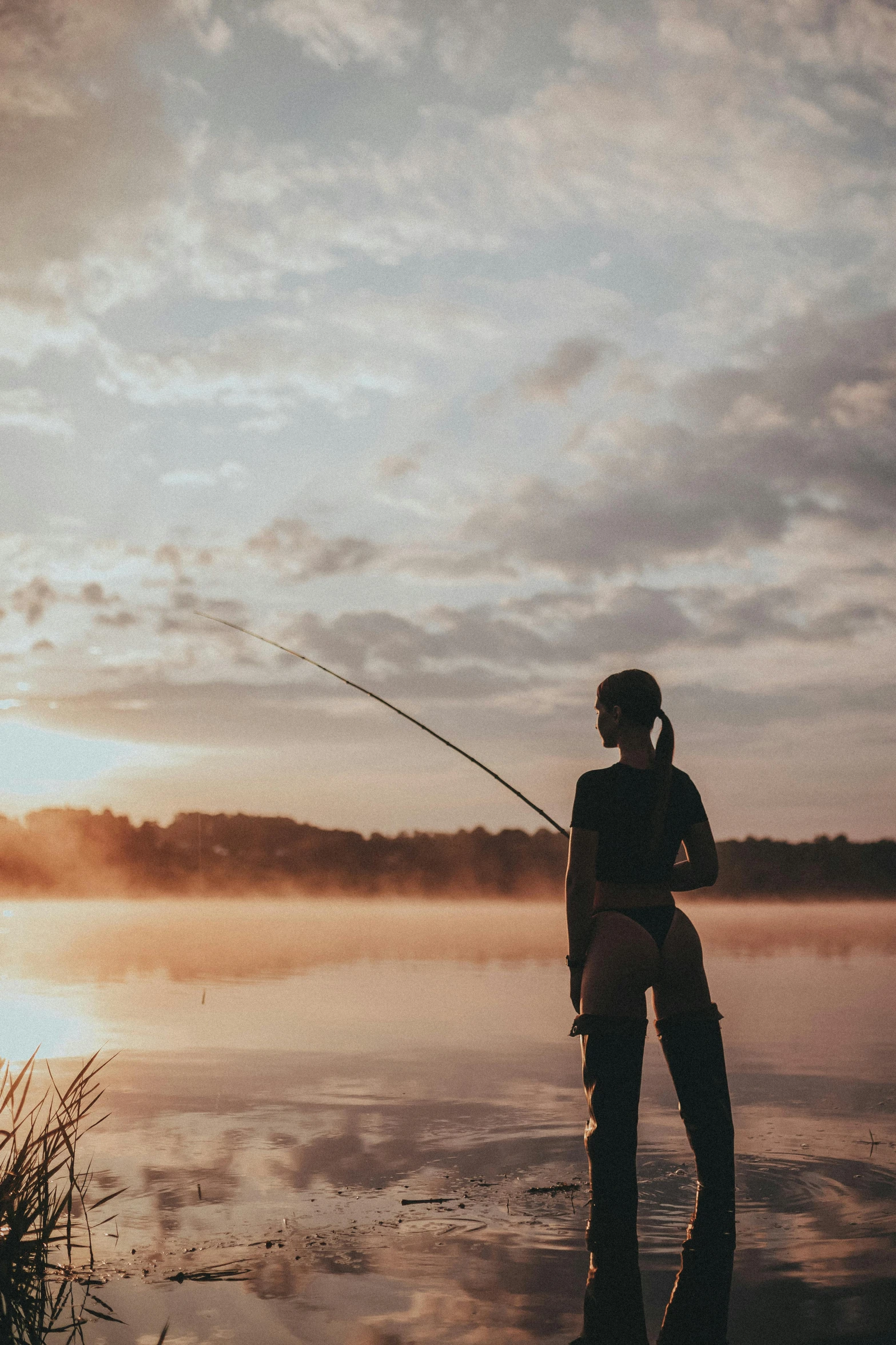 man fishing on a lake in front of the sun