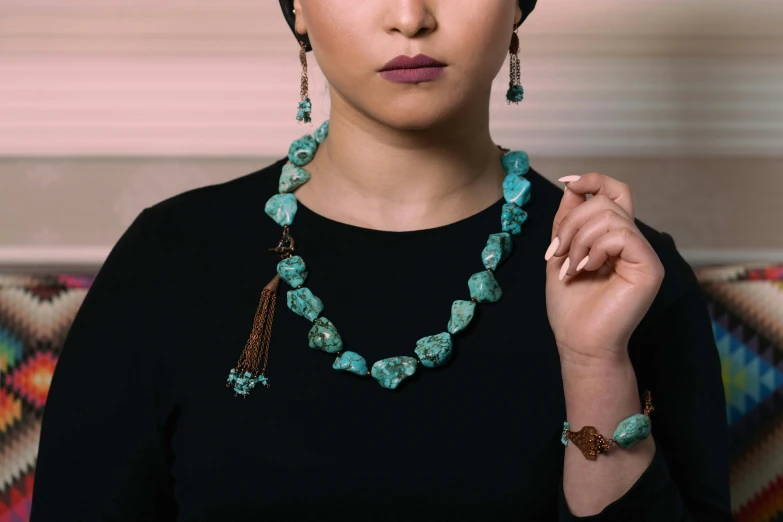 a beautiful woman in black dress holding a green beaded necklace