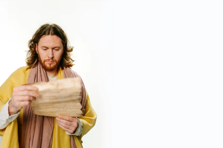 man wearing scarf holding large wooden item in one hand and looking at paper while on other