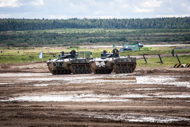 two tanks on the muddy ground next to trees