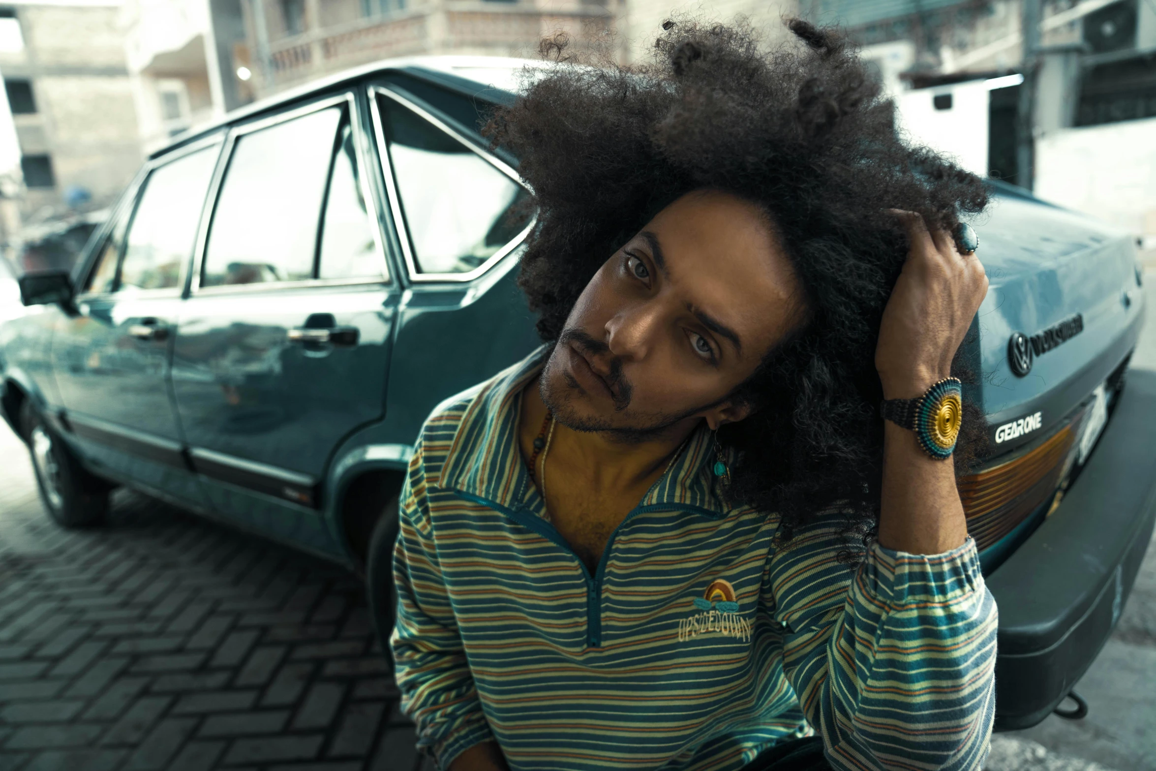 a man with an afro looking at the camera while leaning on a parked car