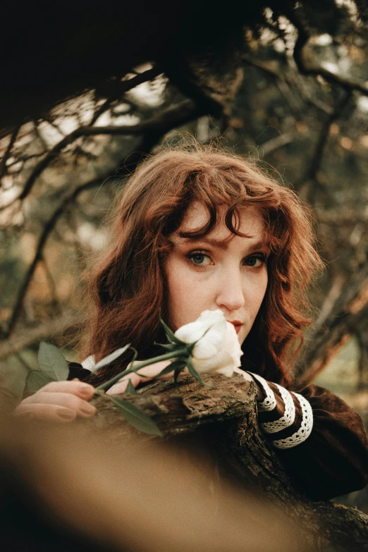 woman putting flower in her mouth and standing under a tree