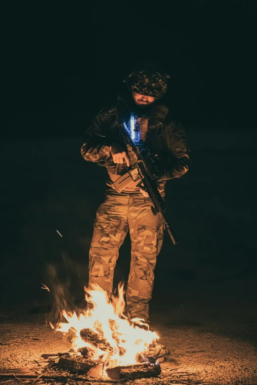 a man is standing next to a fire holding a rifle