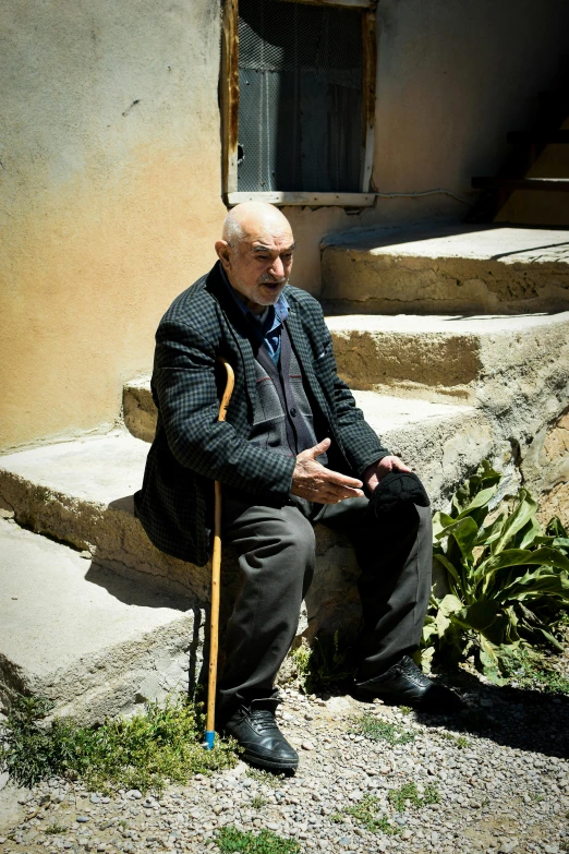an old man is sitting outside holding his cane