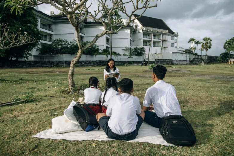 five people sitting on a blanket at the park