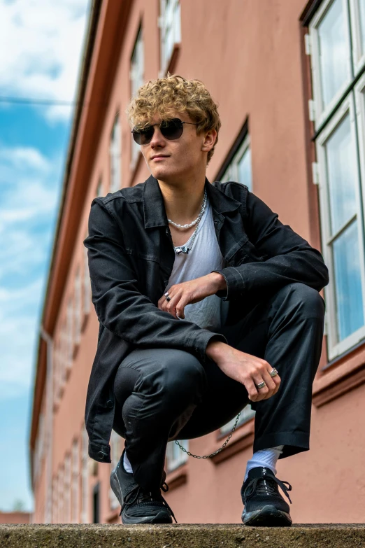 a young man in sunglasses and jacket sitting on steps